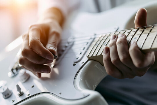 Close up of hands playing white electric guitar with warm sunlight and fretboard detail.