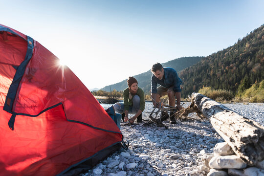 Mature couple camping at riverside, collecting wood for a camp fire