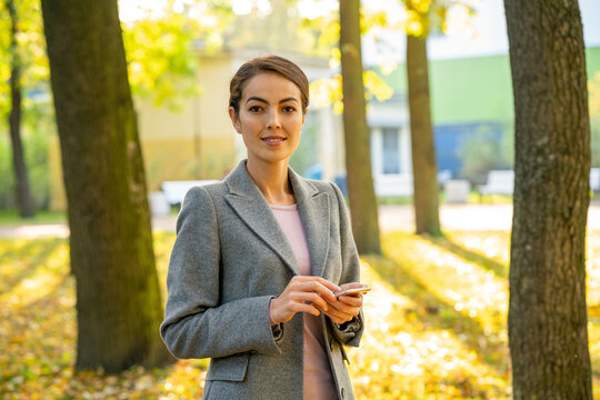 Young female entrepreneur holding smart phone in park during autumn season