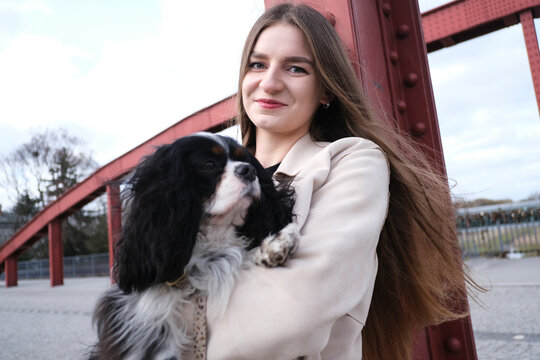A smiling woman holds her cute dog on a red bridge in Poland