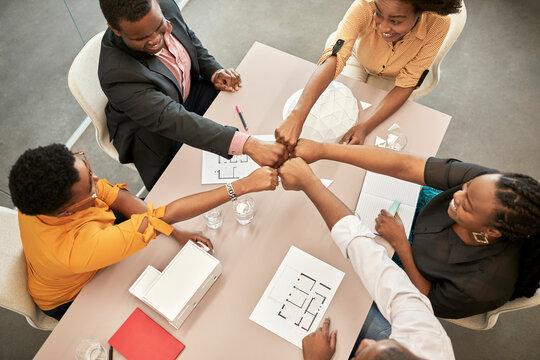Smiling business people doing fist bump at desk during meeting in coworking office