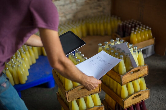 Man with tablet checking stock of juice bottles in warehouse