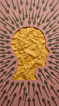 Silhouette of a head profile filled with crumpled gold paper, surrounded by green arrows pointing inward, symbolizing focused thought or external pressure.