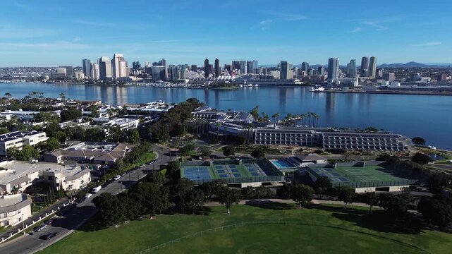 Wide aerial perspective showcases dense residential neighborhoods, community hospital infrastructure, bayfront vistas stretching toward San Diego skyscrapers under clear blue sky in Coronado, CA