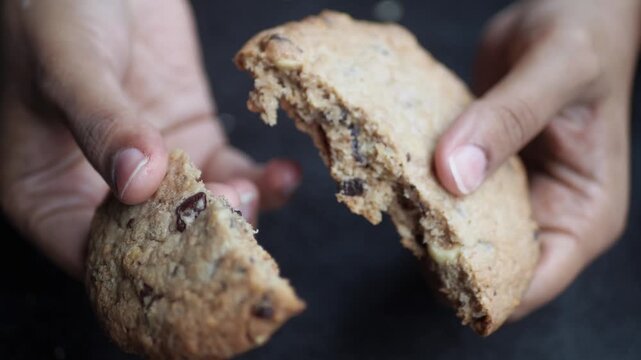 Close-up slow motion video of hands breaking a chocolate chip cookie in half revealing texture