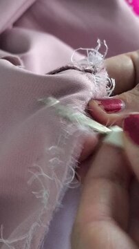 Close up of tailor's hands unpicking seams with seam ripper, clothing repair, sewing process and apparel manufacturing.