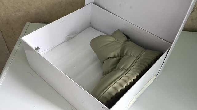 Woman packing shoes into storage box, organizing seasonal footwear at home, shoe storage, packing and home organization concept.