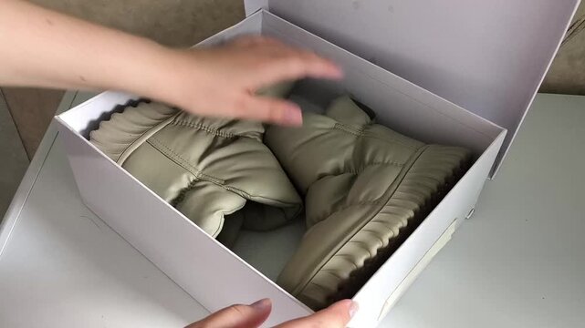 Woman placing shoes into cardboard box for off-season storage, footwear organization, packing and home decluttering.