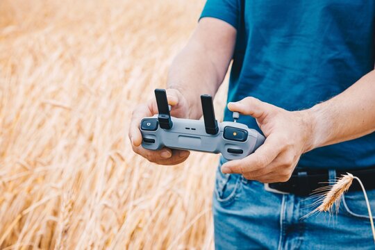 Closeup of pilot hands holding smart drone remote controller with display over a rye field