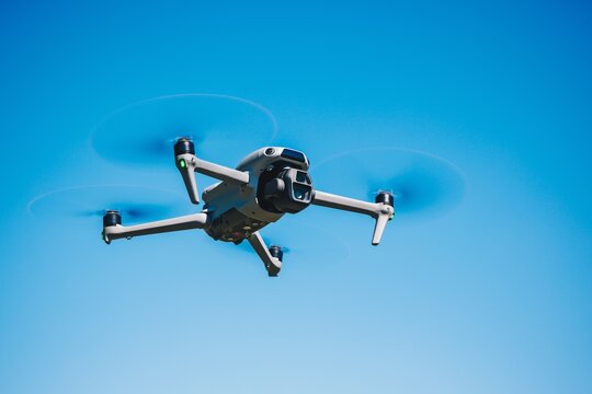 Low angle shot of a modern quadcopter drone hovering in the clear blue sky during daylight