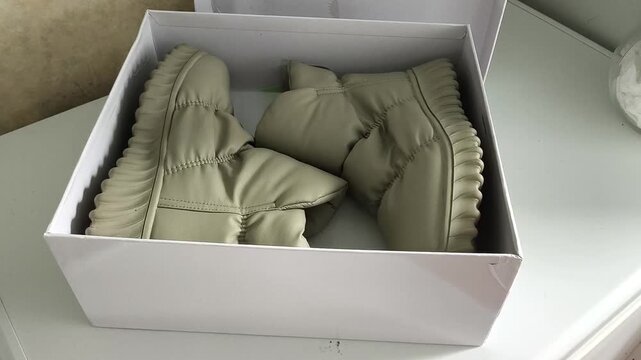 Woman placing shoes into cardboard box for off-season storage, footwear organization, packing and home decluttering.