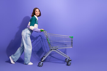 Young stylish woman pushes a shopping cart in a bright purple studio smiling for a fashion lifestyle image © deagreez