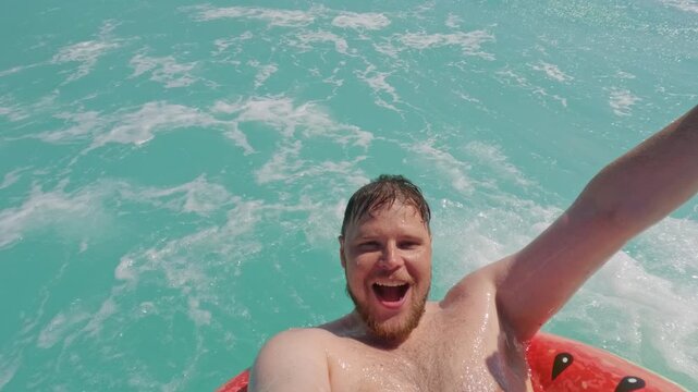 Happy man taking an inflatable ring selfie on turquoise water