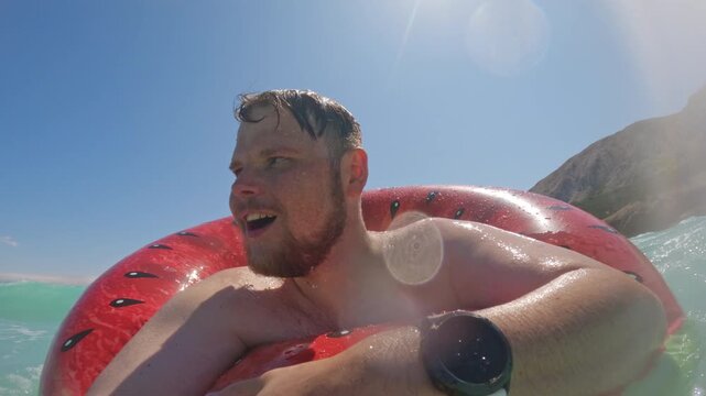 Man in inflatable ring hit by sea splash