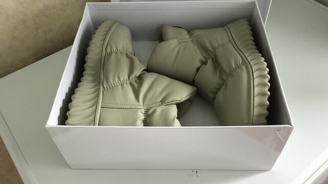 Woman placing shoes into cardboard box for off-season storage, footwear organization, packing and home decluttering.