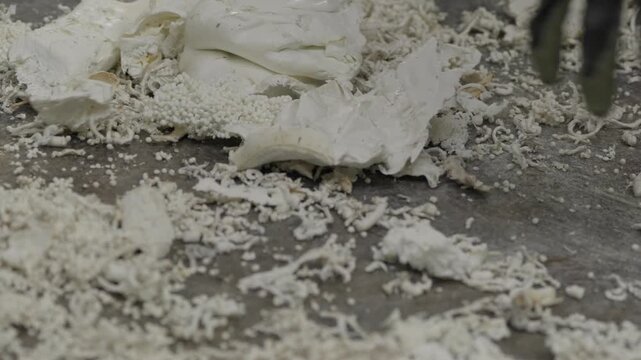 Close up of pulped white plastic waste and shredded fibers spread across concrete floor in recycling plant