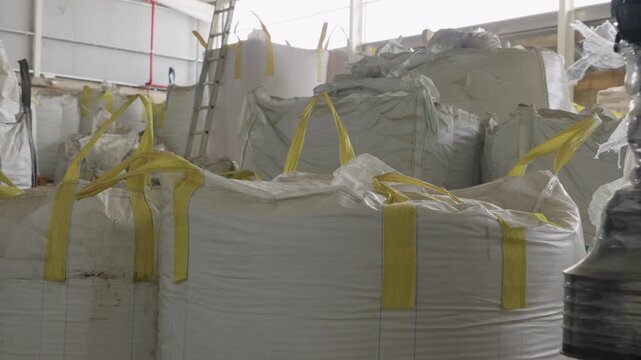 Rows of large white bulk bags with yellow straps filled with plastic waste in recycling warehouse