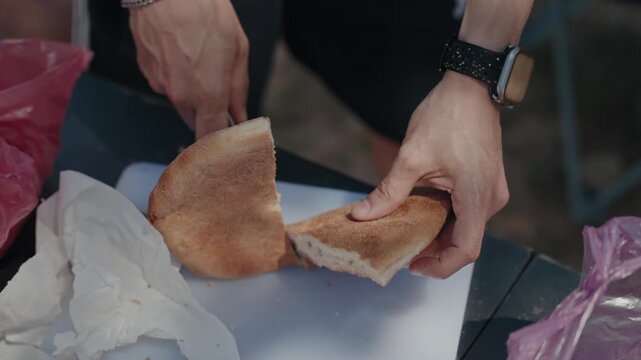 Hands cutting a round crusty bread loaf open with a knife on a white board