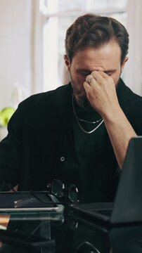 Frustrated, man and headache with stress in barbershop for small business debt or financial crisis. Barber, male person or stylist with glasses, laptop or tablet for eye strain or bankruptcy in salon
