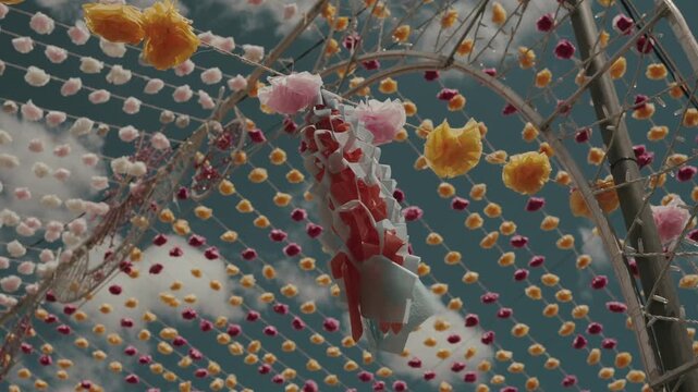 Wire structure supports layers of pompom flowers and bead strings against sky at arraial festival in Portugal