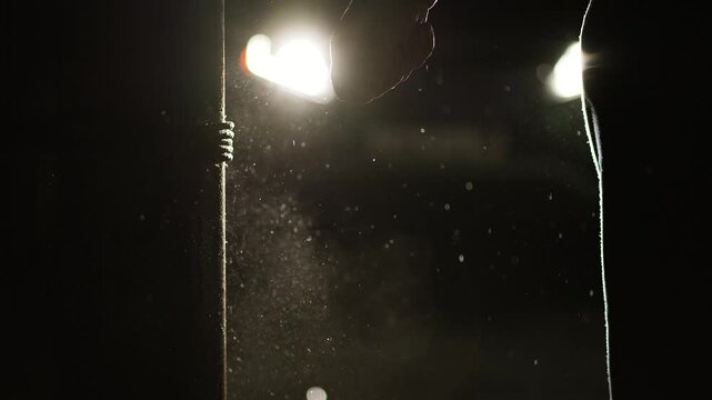 Man smashing a glass bottle in the dark night in bright car headlights