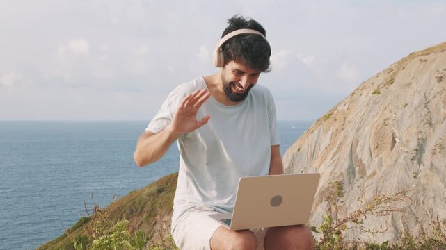Digital nomad video calling with laptop on a cliff with ocean view
