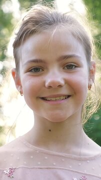Beautiful young girl with amazing green eyes looking at the camera and smiling on a sunny summer day in a park. Happy childhood concept with a child enjoying nature and sunshine outdoors