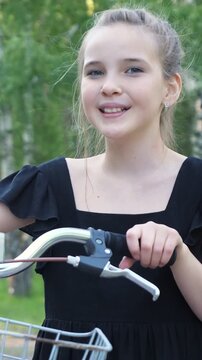 Portrait of a happy pre teen girl with blue eyes standing with her bicycle in a green park, smiling and looking at the camera during a beautiful sunny summer day, enjoying her active lifestyle