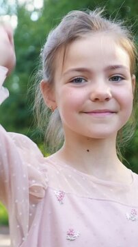 Beautiful little girl with blue eyes smiling at the camera and showing a thumbs up gesture, expressing her positive approval for a beautiful summer day outdoors in a green park