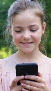 Close up of a happy little girl with freckles enjoying her time outdoors, smiling as she actively uses her mobile phone for texting, browsing social media, or playing games