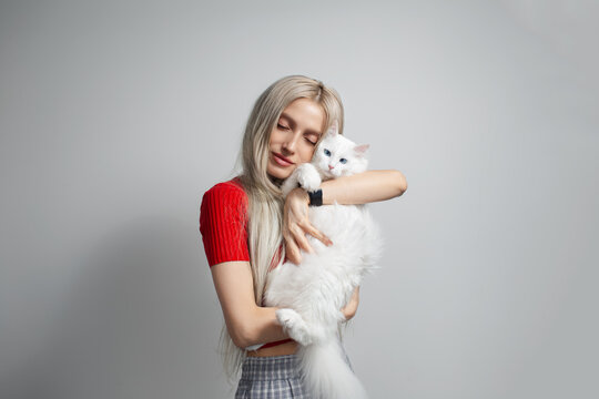 Young blonde girl with fluffy white cat in hands isolated on grey background. Studio portrait.