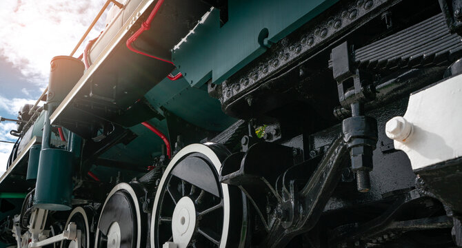 Low angle close up of historic steam locomotive wheels, suspension and mechanical engineering components showing industrial railway technology, transportation machinery and vintage train details.