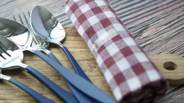 A close-up shot of dinner cutlery set on wooden background, a combination of fork and spoons with napkins on table, dynamic footage