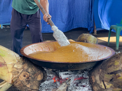 Traditional preparation of jenang or dodol at a Javanese community celebration, showing thick sweet batter being stirred in a large pan over a wood fire, representing Indonesian culinary heritage.