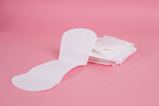 Open Sanitary Pad Leaning Against A Stack Of Folded Pantyliners Isolated On Pink Background