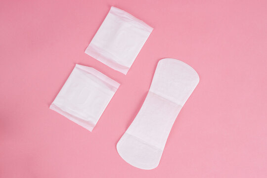 Two Wrapped Sanitary Pads Beside Open Pantyliner Representing Feminine Hygiene Over Pink Background