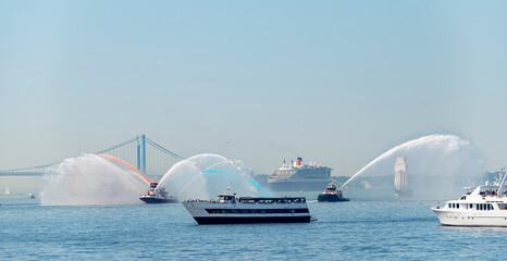 Water salute surrounds cruise ship near Verrazzano Narrows Bridge. Fireboats spray orange and blue...