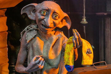 Obraz premium A gray-skinned creature from Harry Potter, sitting on a weathered stone ledge in a dark room with warm, soft lighting Wearing vibrant yellow and blue attire, the cr - Kyiv, Ukraine - June 7, 2025