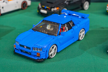 Fototapeta premium Summary Blue Lego sports car on green surface, contrasted by black wheels and white rims Silver roll bar, windshield, and silver-backdrop of additional cars - Kyiv, Ukraine - June 7, 2025