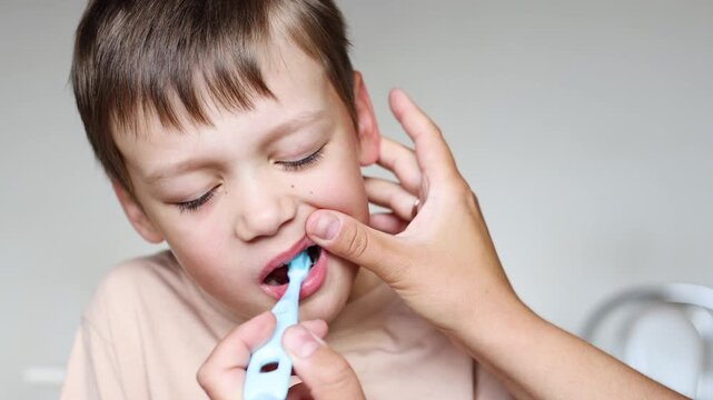 mother hands brushing autistic child teeth. Young boy with autism looks unhappy and resists dental care. Parenting supports oral hygiene habits.