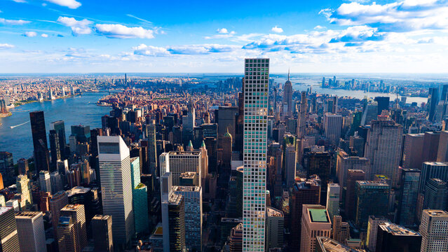 New York City skyline with 432 Park Avenue tower during the day. Aerial view of Manhattan skyscrapers, blue sky with white clouds, East River in the background.