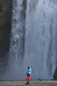 A hiker standing below the towering Skogafoss waterfall, Iceland
