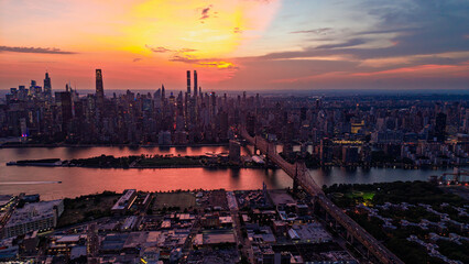 Obraz premium New York City skyline at sunset, view of Manhattan and Queensboro Bridge. Aerial view of the East River and skyscrapers under an orange sky.