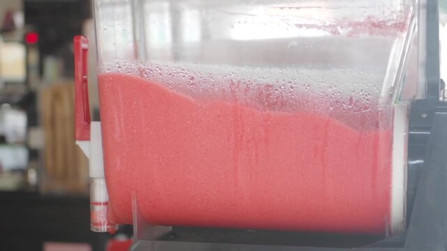 Pink frozen slushy machine spinning with cold strawberry icy beverage in transparent container