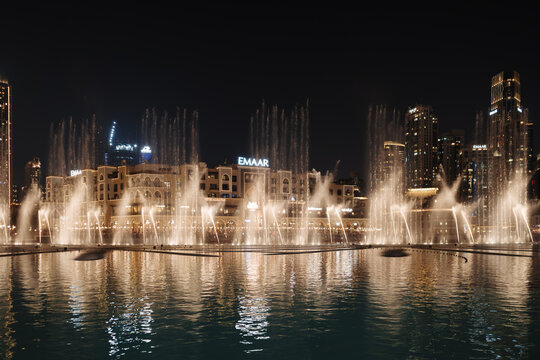 A night view of the illuminated fountains at Dubai Fountain Lake with the EMAAR building and skyscrapers in the background in Dubai, United Arab Emirates.