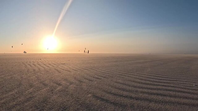 Cinematic coastal storm at sunset with colorful kitesurfers and drifting sand on Kijkduin Beach