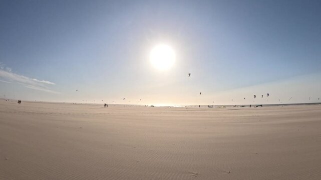 Dramatic golden sunset over Kijkduin Beach with airborne sand and kitesurfing silhouettes