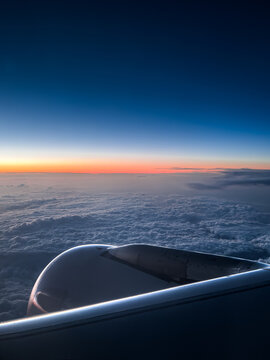 View from an airplane window showing the wing above a sea of clouds at sunrise, with a colorful horizon and peaceful sky during an early morning flight
