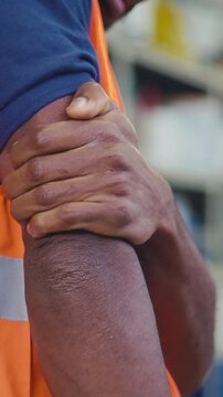 Worker in an orange safety vest experiencing upper arm pain, strain, fatigue, or injury caused by physical labor in workplace settings.