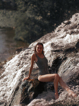 Attractive young woman lying on wet rocks under splashing mountain waterfall stream